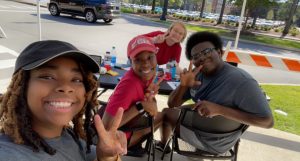 photo of four students flashing peace signs while sitting at a table