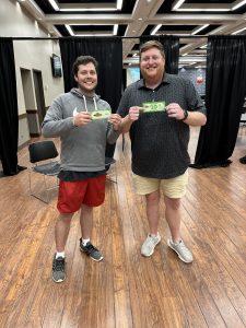 two men holding gift cards pose for a photo