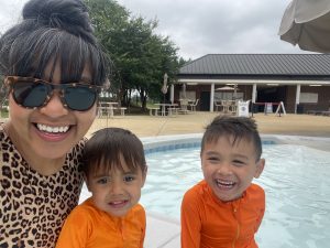 a mom takes a selfie with her two young children with a pool in the background