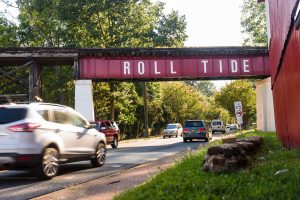 cars passing under a bridge with a sign that says roll tide