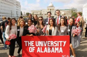 a large group of students stand and hold a university of alabama sign in washington d.c. with capital hill in the background